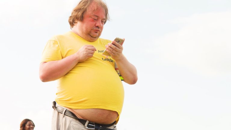 man in yellow shirt and brown pants using smartphone